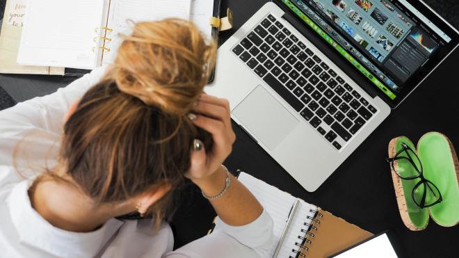 A person sits in front of a laptop with their head bowed.